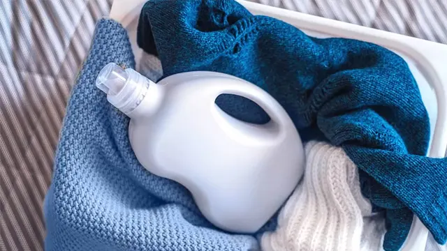 Cesta de ropa con prendas de diferentes tejidos y una botella de detergente