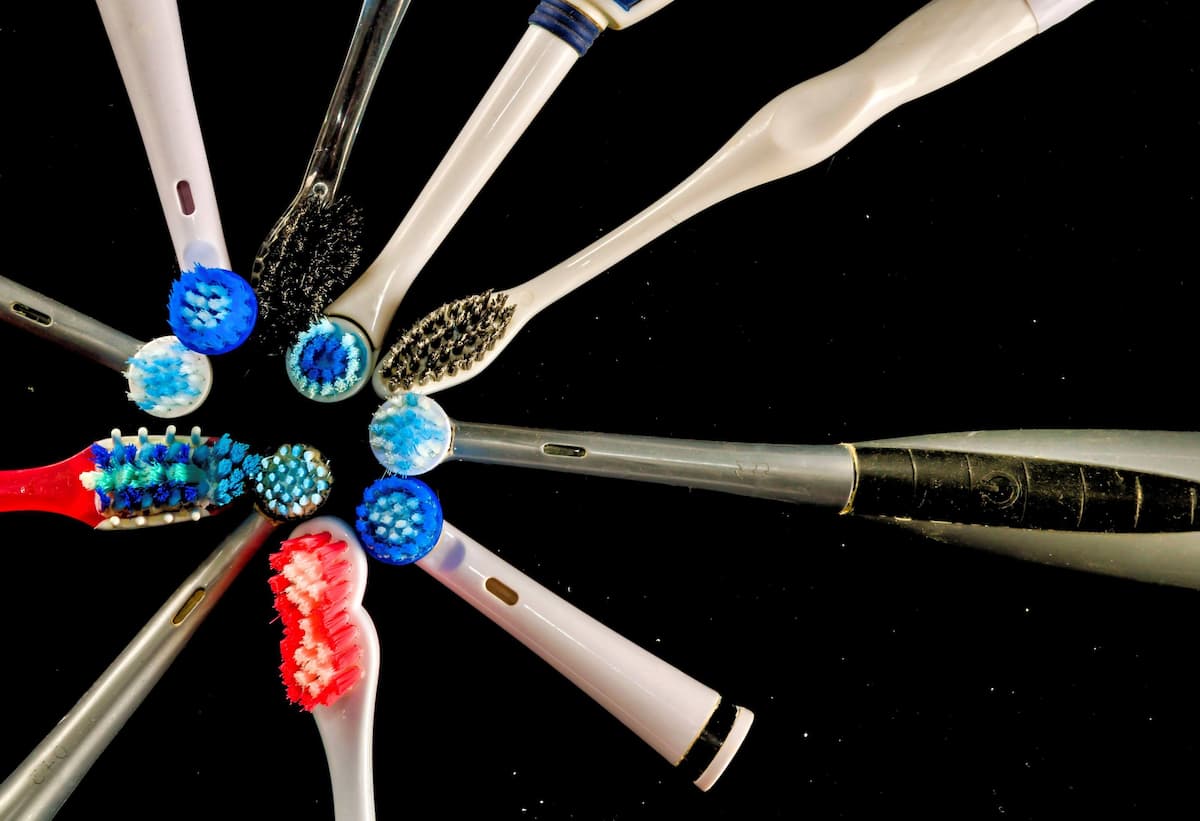 Varios cepillos de dientes eléctricos de distintos modelos y colores dispuestos en forma radial con los cabezales al centro, sobre fondo negro.