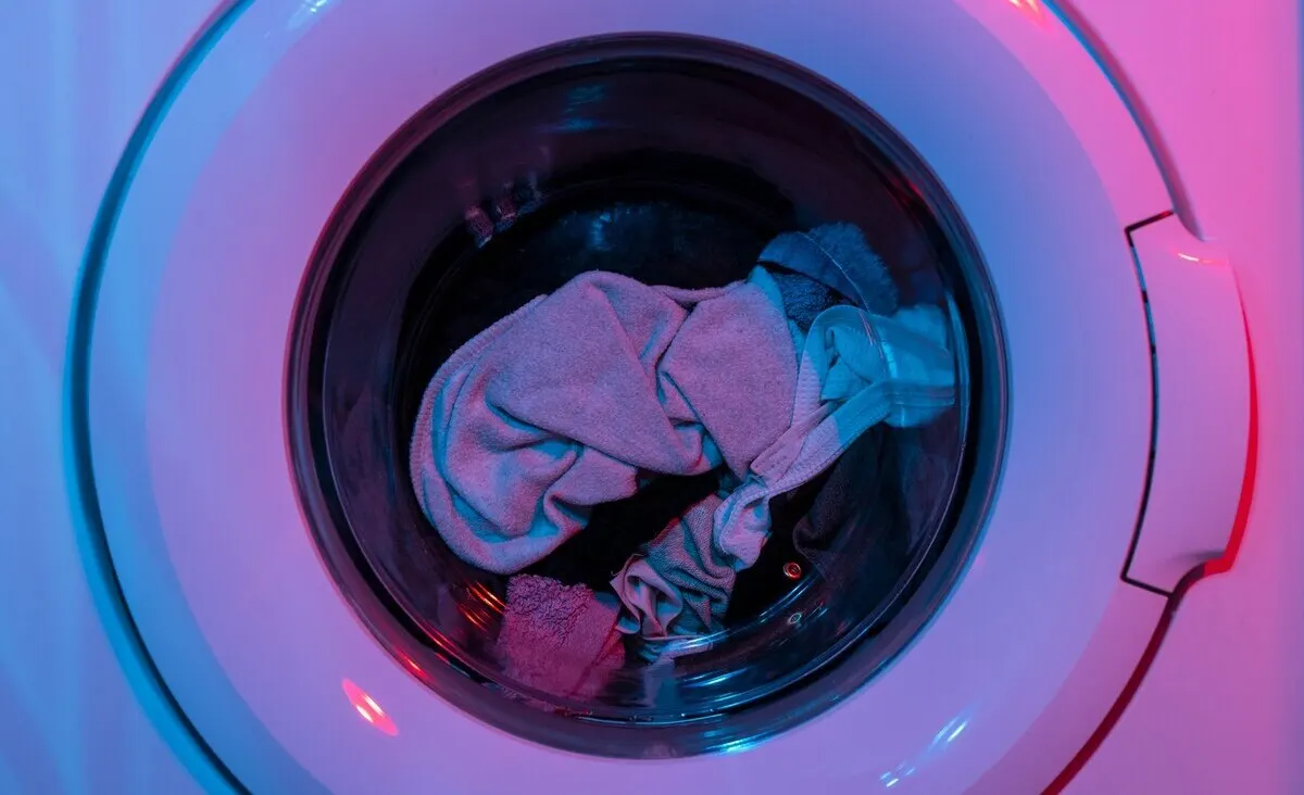 Lavadora blanca con ropa dentro del tambor metálico. La iluminación es azul y rosa.