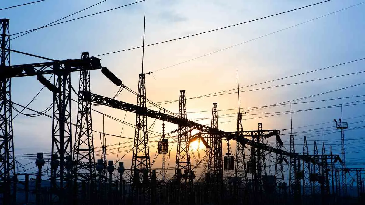 Siluetas de torres eléctricas y cables contra un cielo al atardecer con tonos azules y anaranjados.