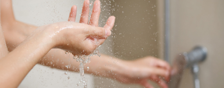 Mano abierta bajo el agua que cae en una ducha con grifo metálico al fondo.