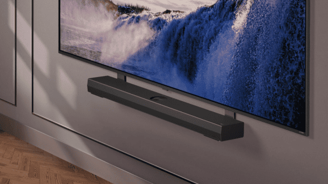 Televisor con cascada azul y blanca, y barra de sonido negra debajo, montados en una pared gris con molduras.