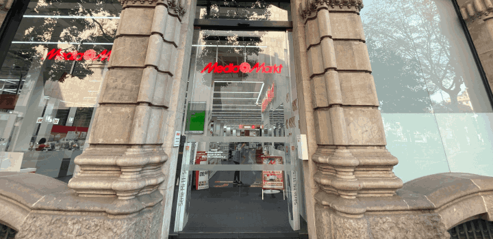 Entrada de tienda con columnas de piedra a ambos lados. Puerta de cristal con el logo rojo "Media Markt". Se ven estanterías dentro.