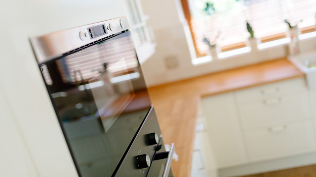Horno moderno con panel de control metálico y mandos negros, junto a una ventana en una cocina luminosa.