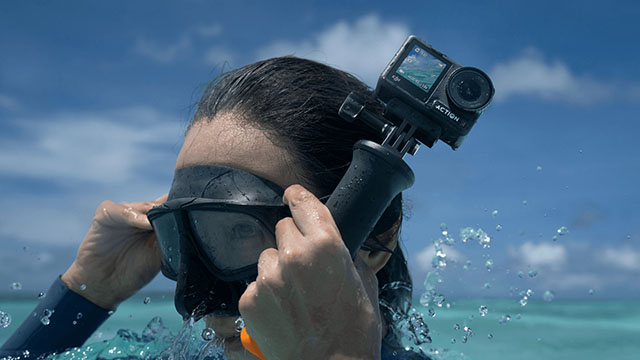 Persona con gafas de buceo sujeta una cámara de acción sobre el agua azul clara.