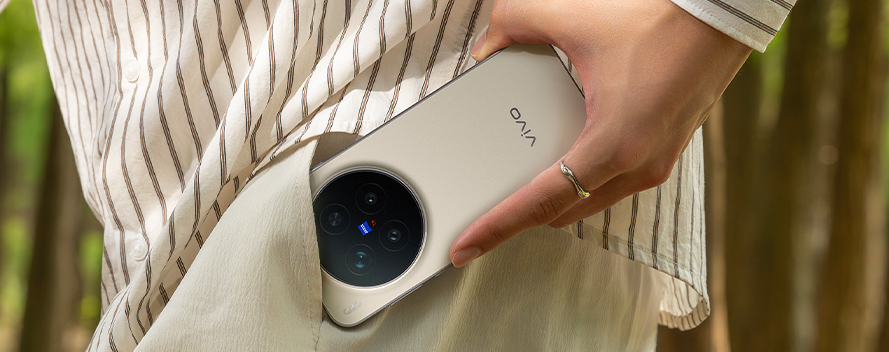 Persona con camisa de rayas beige y pantalón claro guarda un smartphone vivo beige en el bolsillo, destacando diseño delgado, elegante y cómodo de llevar en el día.