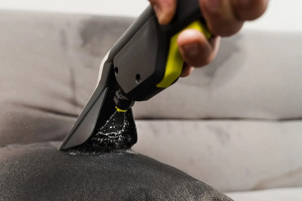 Boquilla de limpiatapicerías aplicando agua a un sofá.