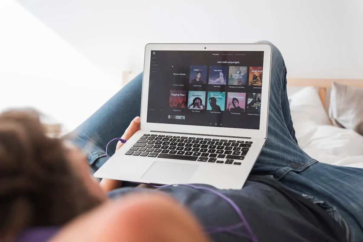 Persona recostada usando portátil para escuchar música en la cama.