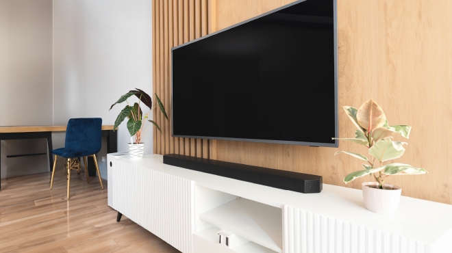 Un salón muestra una televisión, una barra de sonido negra, un armario blanco, dos plantas y una silla azul.