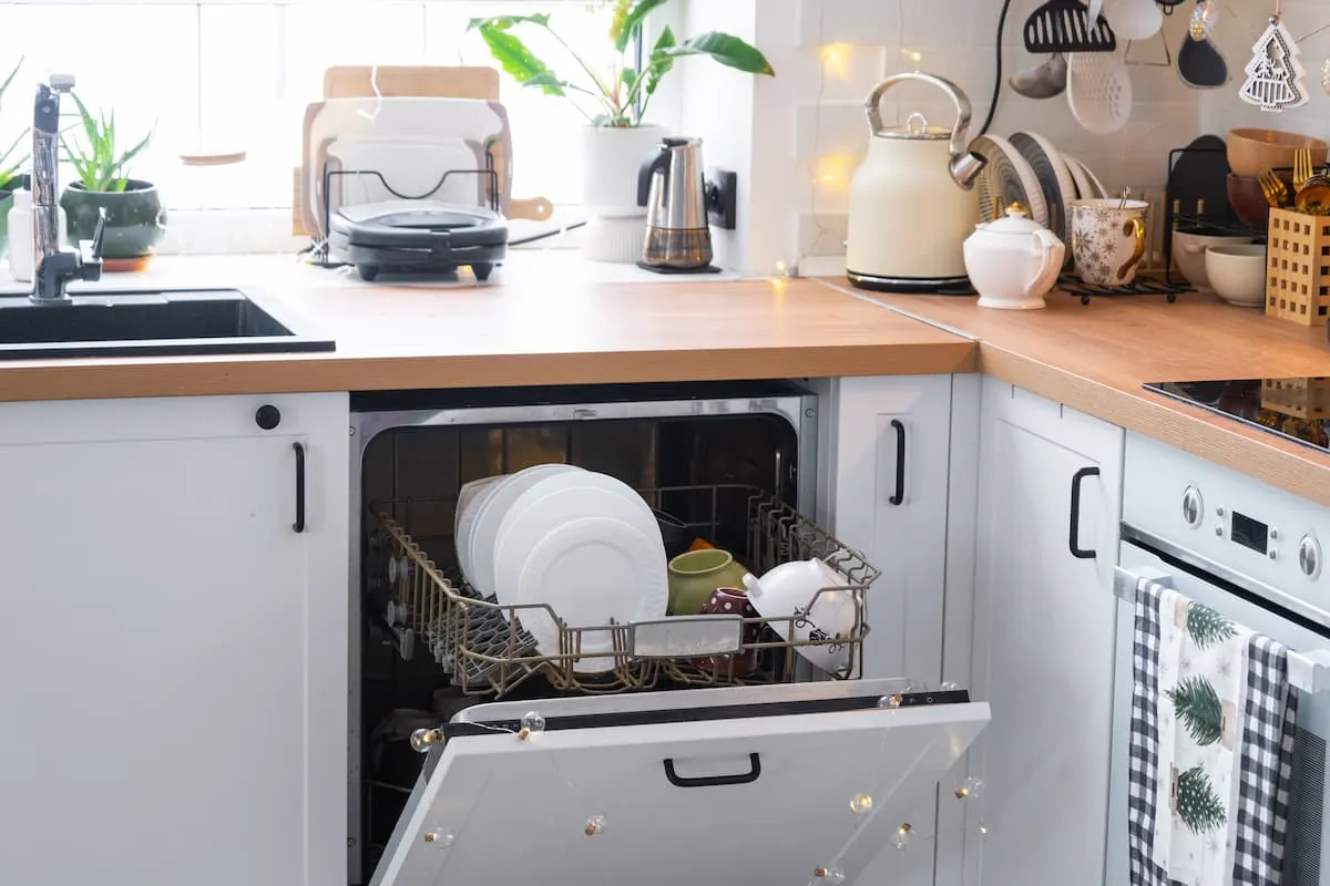 Lavavajillas empotrado abierto con platos limpios en cocina blanca con encimera de madera.