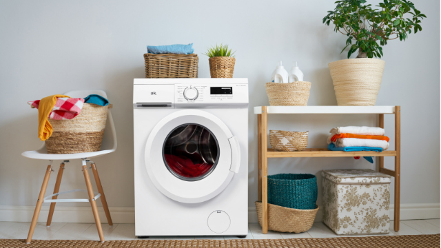 Lavadora OWM 6143 D de ok. en un lavadero moderno, rodeada de cestas de ropa, toallas y plantas.