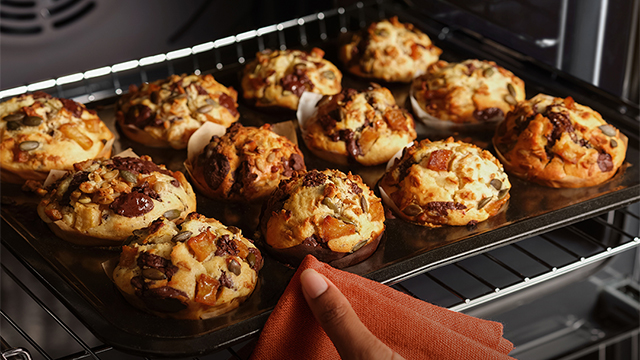Una mujer extrae una bandeja con repostería del horno de maneras sencilla y práctica gracias a los raíles telescópicos. 