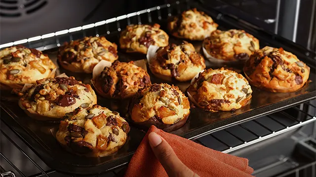 Una mujer extrae una bandeja con repostería del horno de maneras sencilla y práctica gracias a los raíles telescópicos.