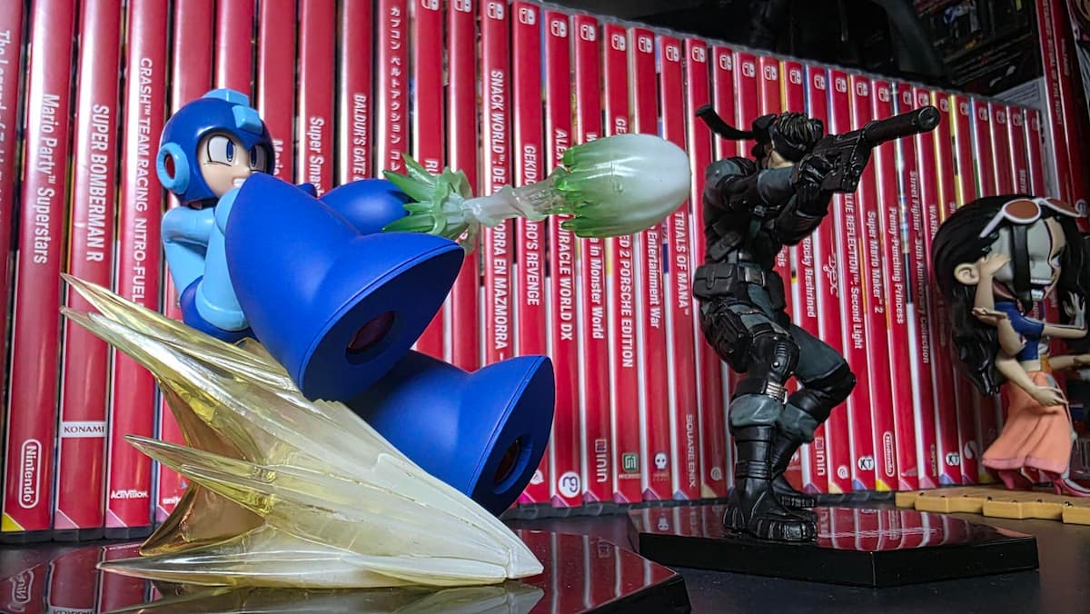Figuras de Mega Man y un soldado táctico frente a una fila de videojuegos de Nintendo Switch en una estantería.