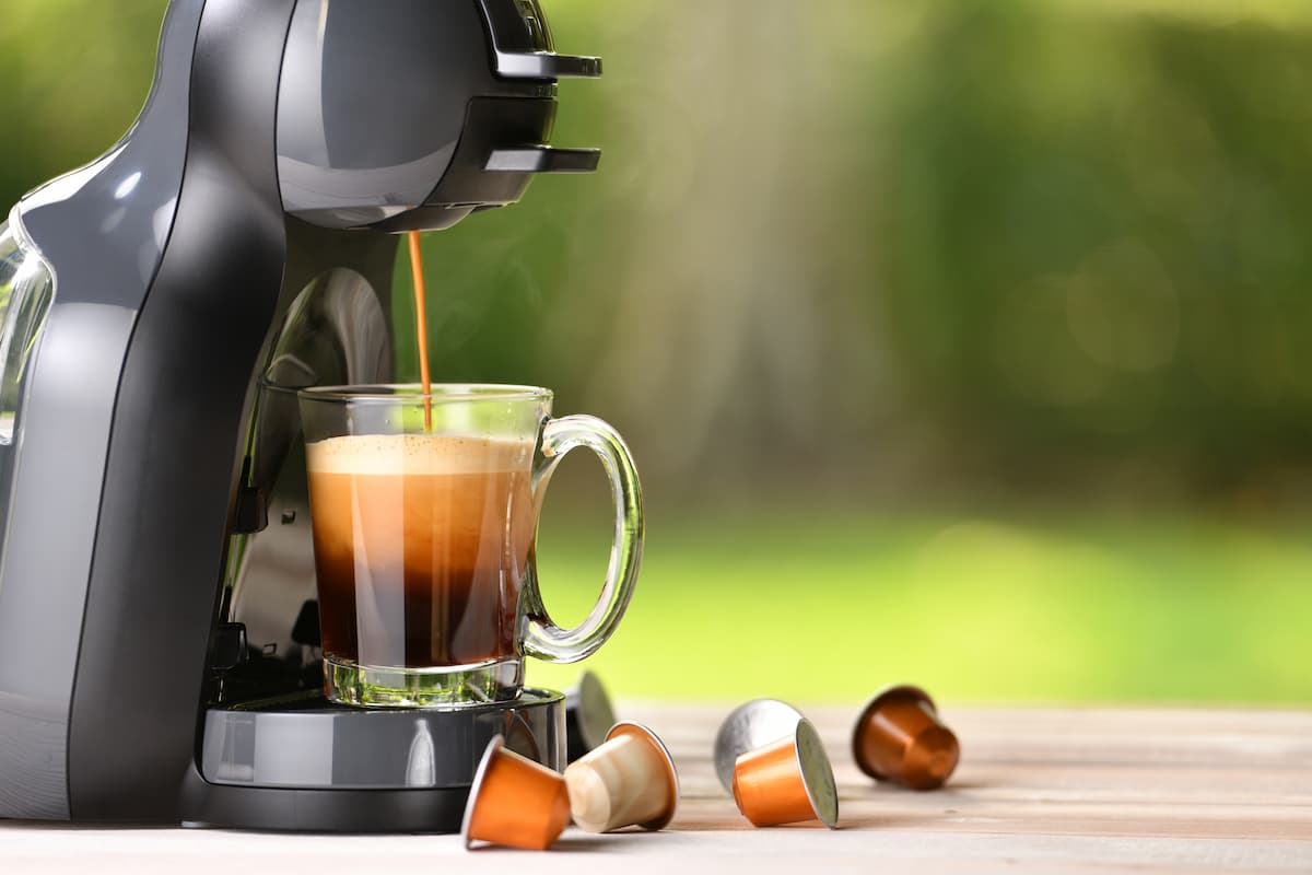 Cafeteran Dolce Gusto de cápsulas sirviendo espresso en taza de vidrio con cápsulas alrededor