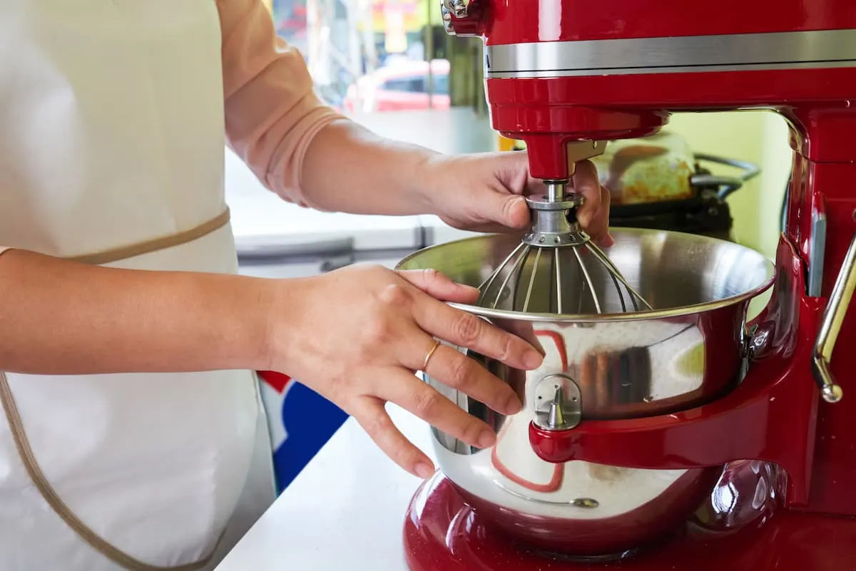 Persona ajustando el tazón de acero de una batidora de pedestal roja en una cocina.