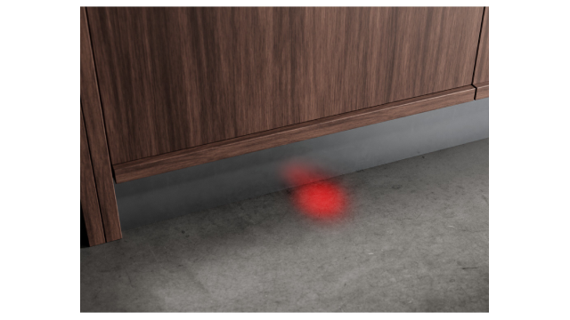 Un panel de madera con una luz roja proyectada sobre el suelo que indica que el lavavajillas está en funcionamiento.