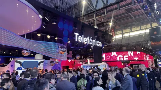 Feria con stands de Telefónica y Magenta, con mucha gente. Hay techos altos y luces brillantes.