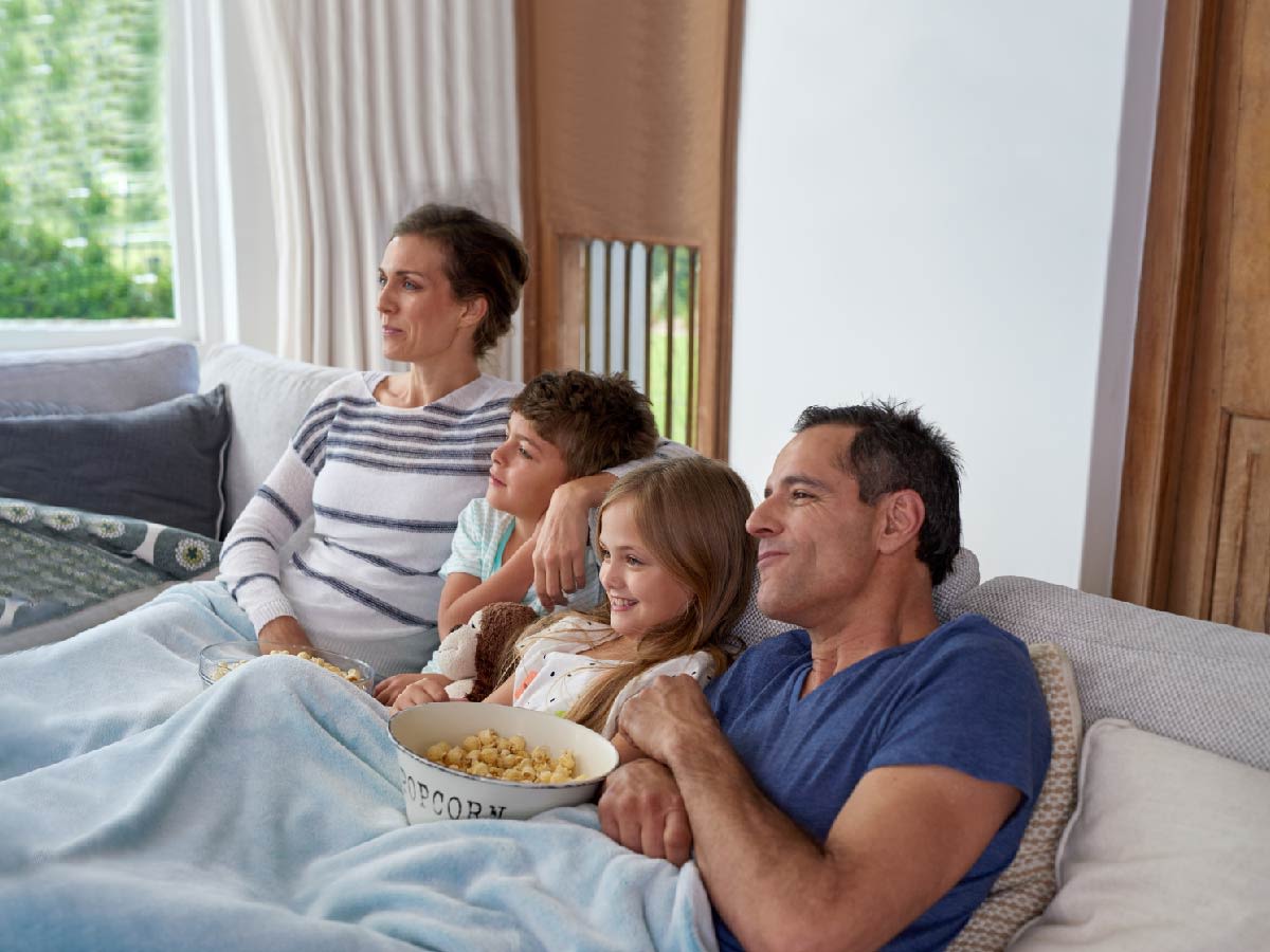 Familia sentada en el sofá viendo una película y compartiendo un bol de palomitas.