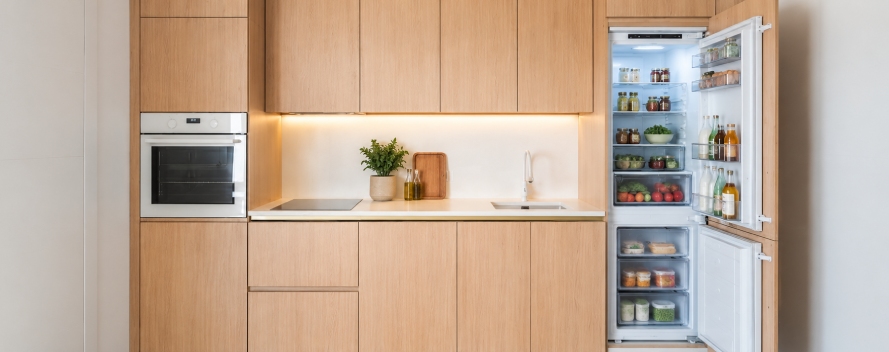 Cocina moderna de madera , hombre abre nevera llena de alimentos y una planta decorativa sobre la encimera