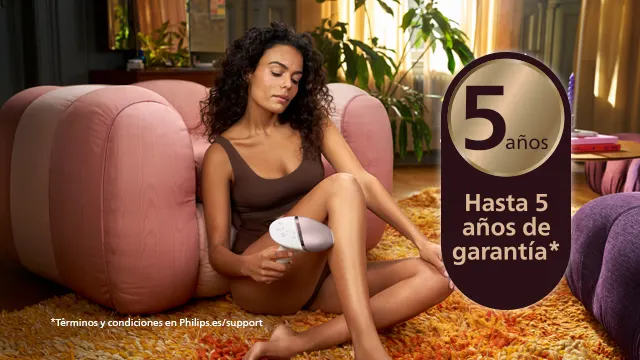 Mujer sentada en un sillón rosa usando un dispositivo blanco en su pierna. Un texto anuncia "5 años de garantía".