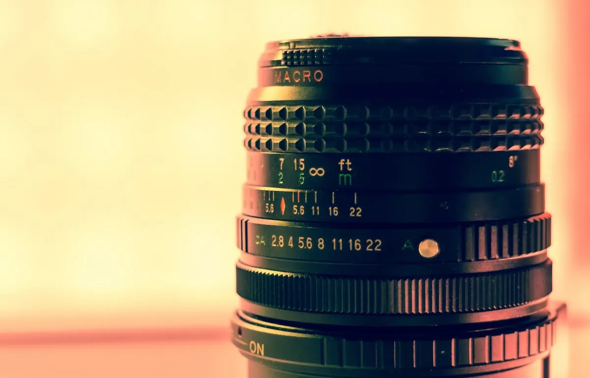 Primer plano de un objetivo de cámara negro con fondo desenfocado de tonos cálidos.