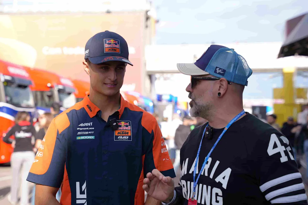 Dos personas conversando en el paddock del MotoGP de Valencia, una de ellas con mono del equipo de motos.