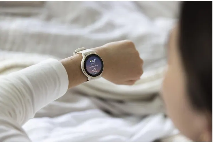 Persona revisando un smartwatch blanco en su muñeca mientras está recostada en la cama.