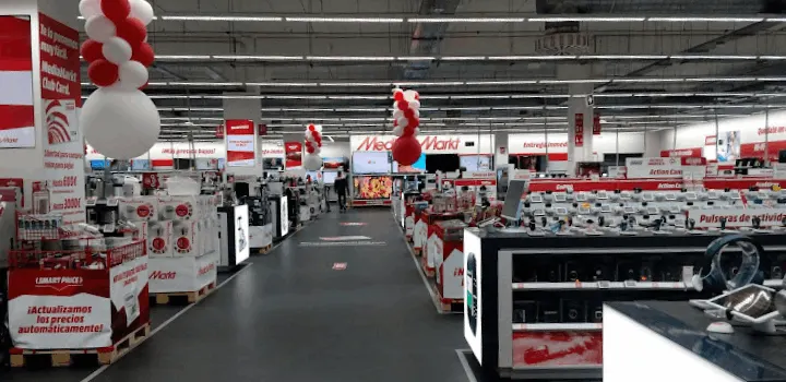 Interior de tienda con pasillo central, estanterías a ambos lados y globos rojos y blancos colgando del techo.