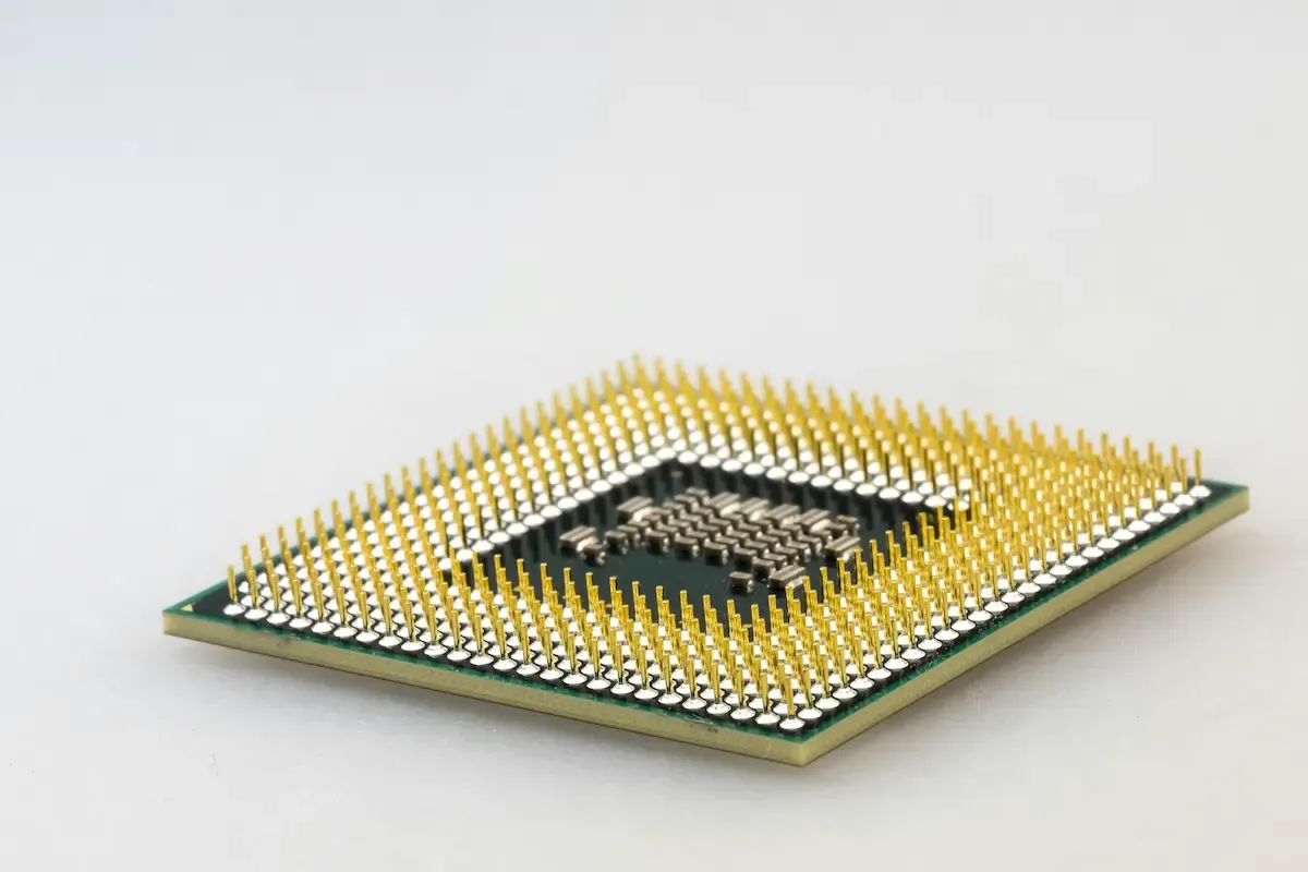 Un chip cuadrado de computadora con pines dorados que sobresalen sobre una superficie blanca.