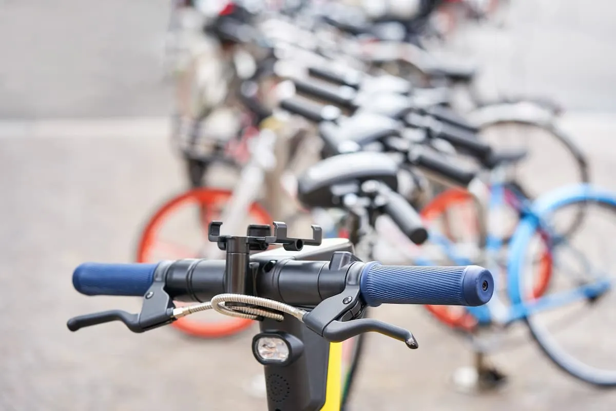 Manillar de una bicicleta compartida en primer plano, con una fila de bicicletas estacionadas al fondo.
