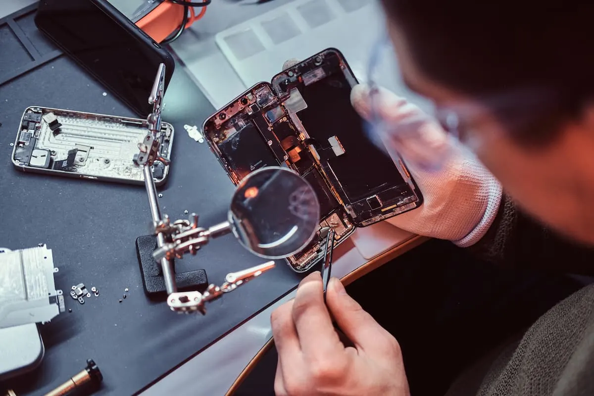 Técnico reparando un teléfono móvil con lupa y herramientas.