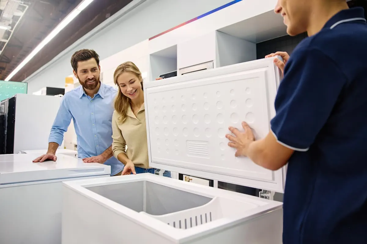 Pareja viendo un arcón congelador abierto con ayuda de un vendedor.