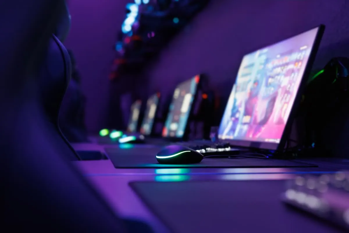 Estación de juego con mouse RGB y monitores en un ambiente de luz púrpura.