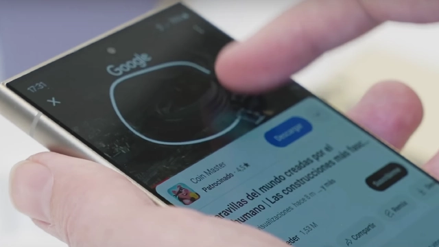 Unas manos sostienen un teléfono móvil con la pantalla encendida mostrando una búsqueda de Google y contenido en español.