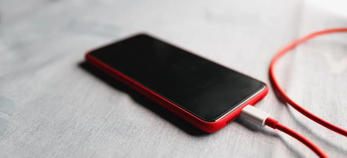 Smartphone rojo cargándose con cable USB-C sobre superficie gris