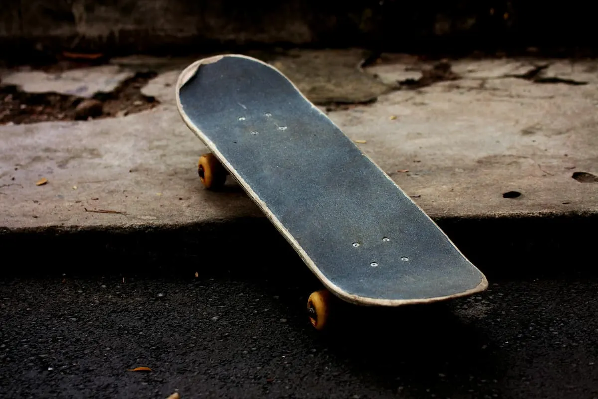 Skateboard desgastado sobre la acera junto a un bordillo urbano.