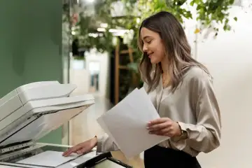 Una mujer está usando una fotocopiadora en una oficina moderna con plantas decorativas