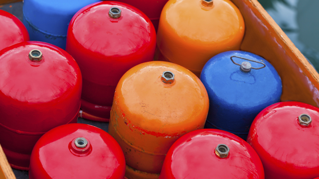 Conjunto de tanques de gas rojos, naranjas y azules en un recipiente, vistos desde arriba en un entorno exterior.