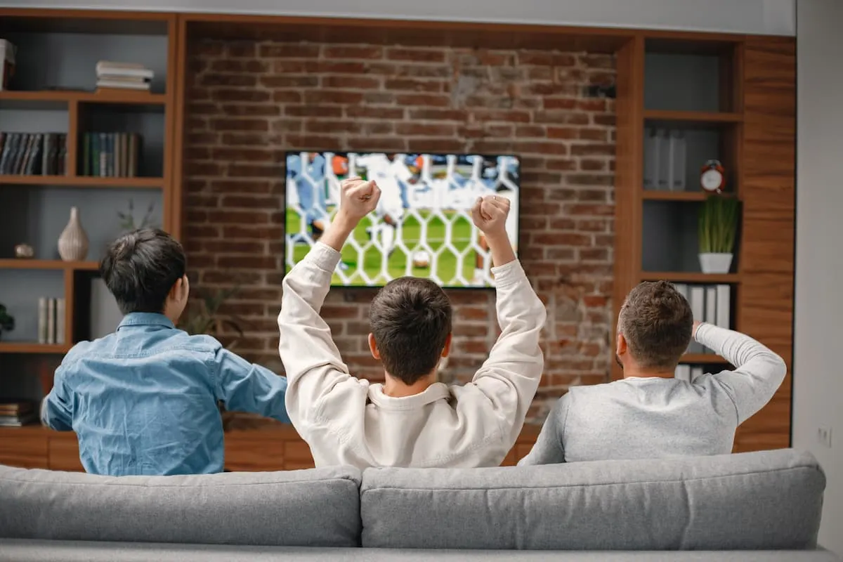 Tres personas viendo fútbol en un televisor de gran pantalla desde el sofá del salón