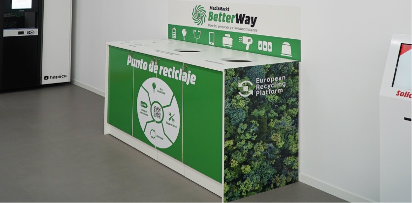 Una persona con camisa roja abre una caja de cartón en una oficina con estantes, impresora, y un monitor de ordenador.