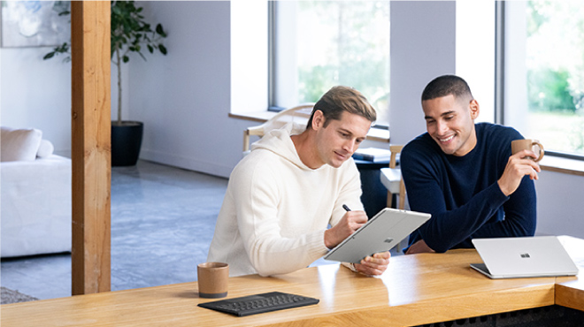 Escritorio blanco con portátil, monitor mostrando datos, teclado, ratón, lámpara dorada y planta en maceta.