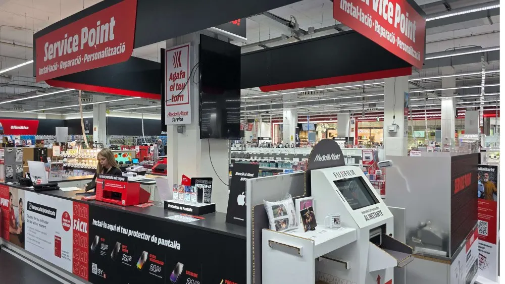 Mostrador del Service Point de MediaMarkt dentro de la tienda, con cartelería roja y negra, zona de reparación e instalación de protectores de pantalla y una especialista atendiendo a los clientes.