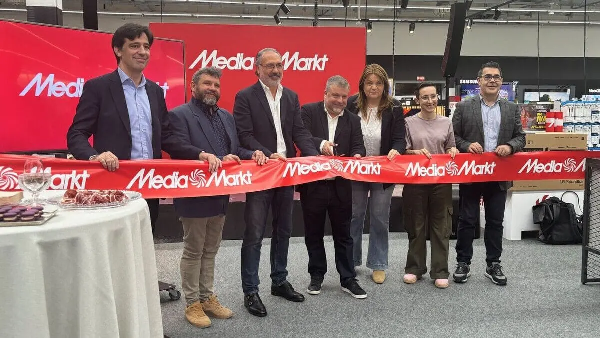 Grupo de personas cortando una cinta roja de "Media Markt" en una tienda con productos electrónicos al fondo.