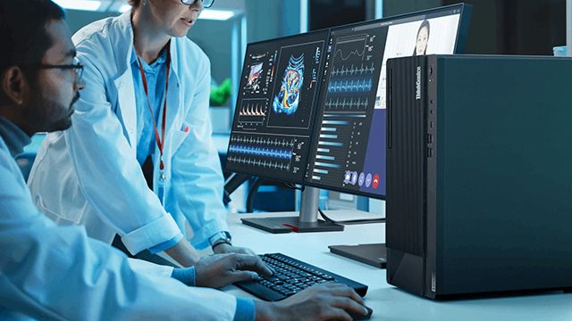 Dos médicos con batas blancas trabajando en computadoras que muestran gráficos e imágenes médicas. Teclado negro visible.