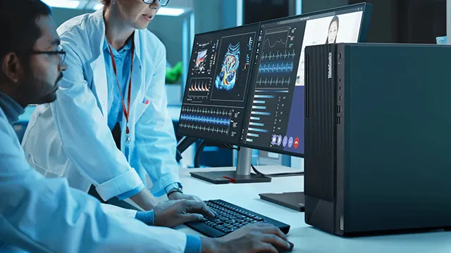 Dos médicos con batas blancas trabajando en computadoras que muestran gráficos e imágenes médicas. Teclado negro visible.