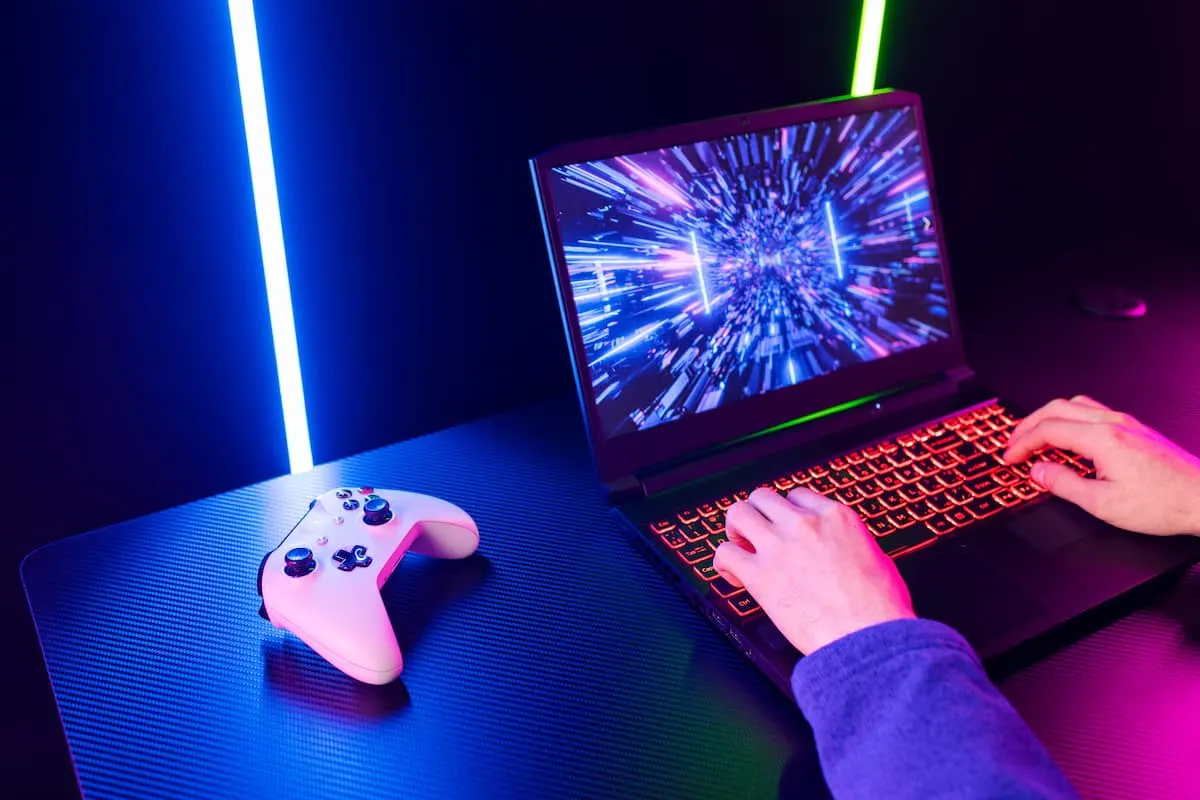 Persona jugando en portátil gaming con mando y luces LED.