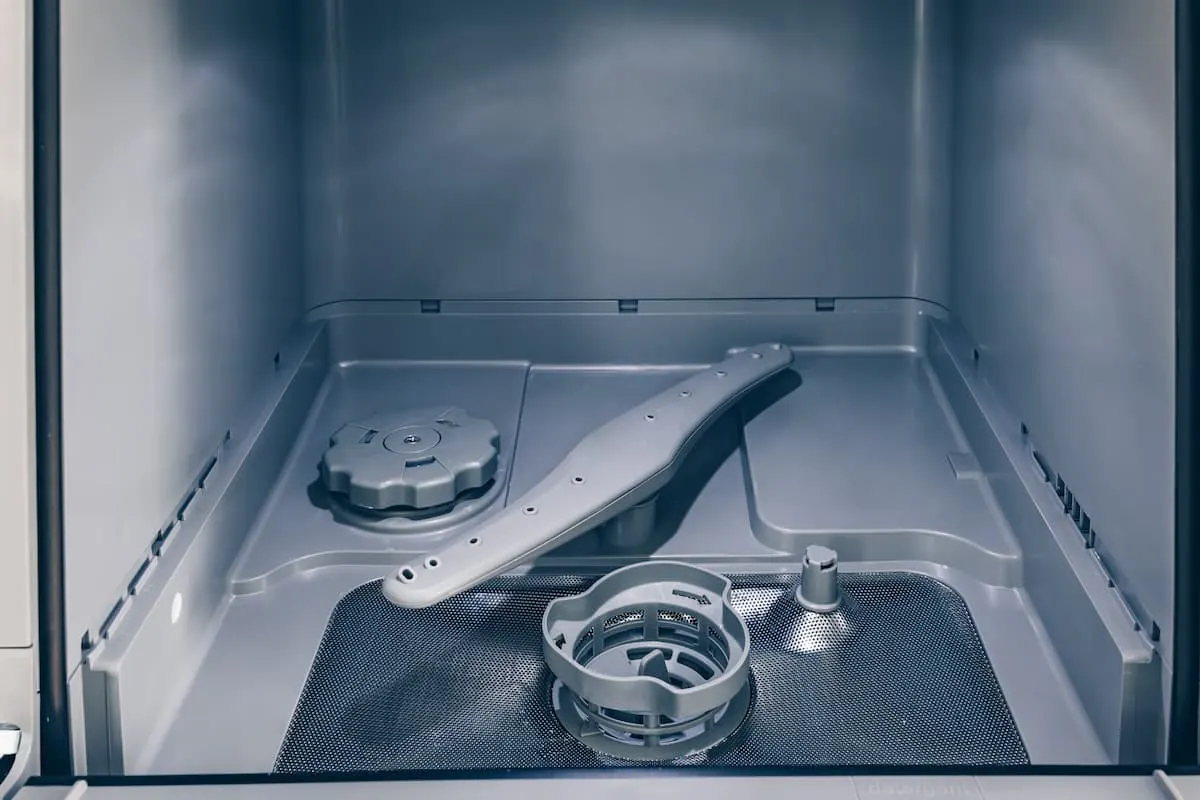Interior vacío de un lavavajillas con el brazo aspersor y piezas desmontadas en el fondo