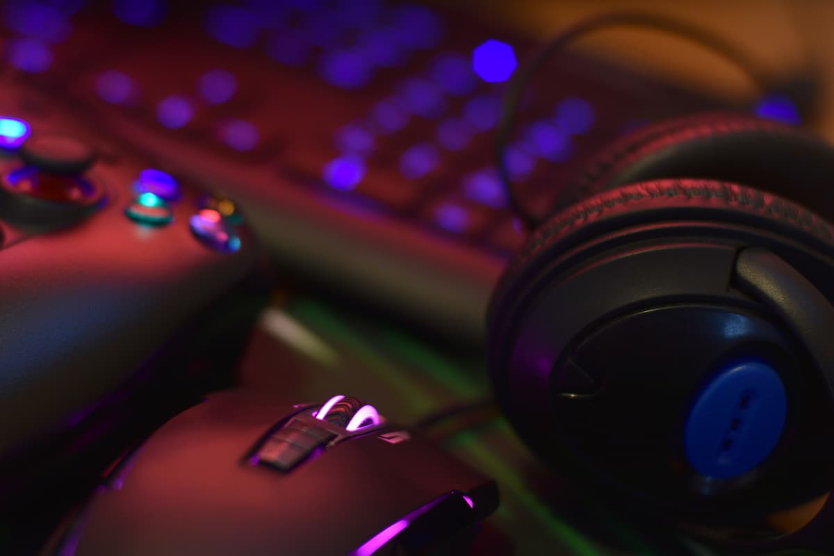 Auriculares, ratón y mando gaming sobre teclado iluminado con luces de colores.