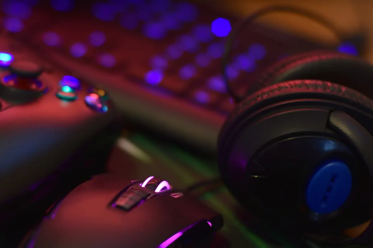 Auriculares, ratón y mando gaming sobre teclado iluminado con luces de colores.